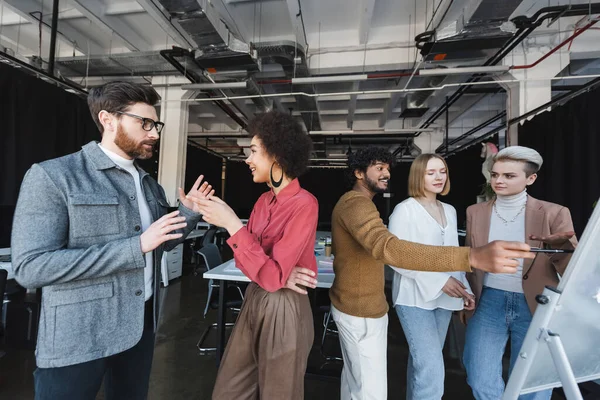 Hombre indio señalando el rotafolio durante la discusión con colegas multiculturales en la agencia de publicidad — Stock Photo