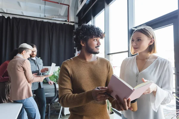 Gérants de publicité interracial se regardant près d'un ordinateur portable tout en parlant au bureau — Photo de stock