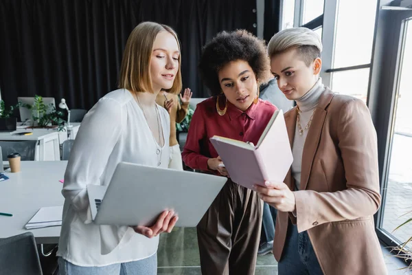 Donne d'affari interrazziali con notebook e laptop che lavorano insieme in agenzia pubblicitaria — Stock Photo