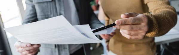 Partial view of man pointing with pen at papers near colleague in advertising agency, banner — Stock Photo