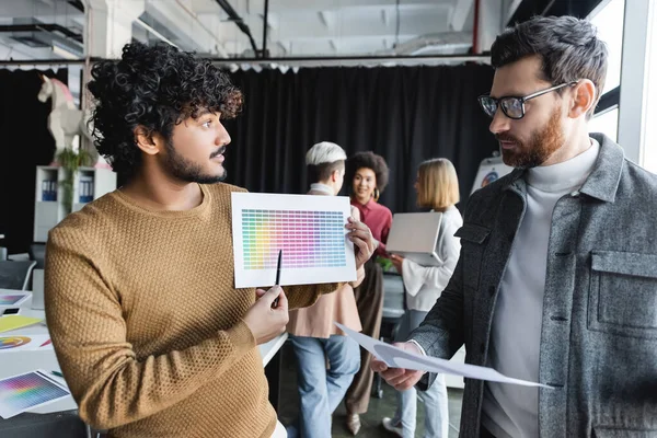 Indian designer pointing at color samples during discussion with colleague in advertising agency — Stock Photo