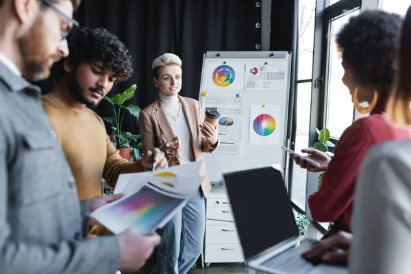 Manager pubblicitari multietnici che parlano vicino a flip chart con progetto in ufficio — Foto stock