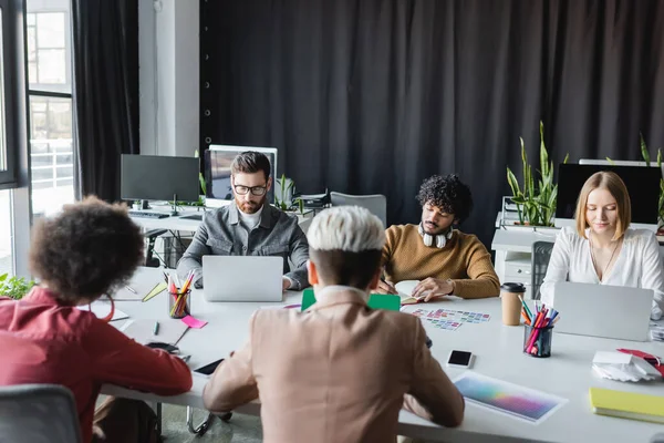 Gerentes de publicidad multicultural que trabajan cerca de ordenadores portátiles en la sala de reuniones - foto de stock