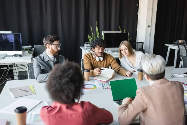 Indischer Mann mit Kopfhörern, der multiethnischen Werbemanagern Farbmuster zeigt — Stockfoto