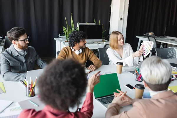 Advertising designer showing color samples to multiethnic coworkers in meeting room — Stock Photo