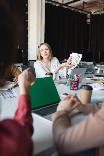 Woman pointing at color samples near blurred multicultural colleagues in advertising agency — Stock Photo