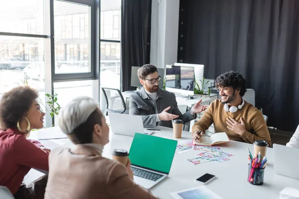 Uomo con gli occhiali che indica un collega indiano soddisfatto durante l'incontro con i manager pubblicitari — Foto stock