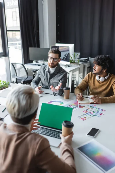 Hombre con anteojos hablando con diseñadores de publicidad multicultural en la sala de reuniones - foto de stock