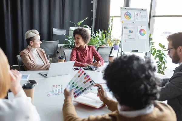 Lächelnde interrassische Frauen im Gespräch mit Kollegen in Werbeagentur — Stockfoto