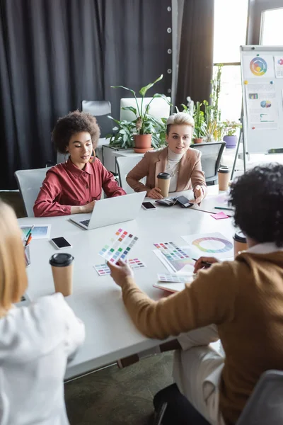 Woman with paper cup talking to multicultural designers in advertising agency — Stock Photo