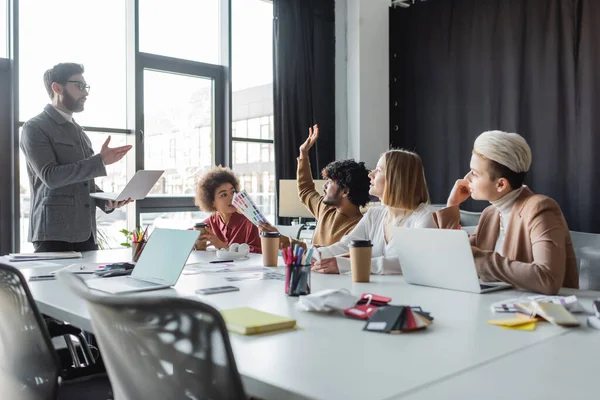 Uomo indiano con campioni di colore alzando la mano durante l'incontro con il team multietnico in agenzia pubblicitaria — Foto stock