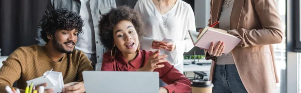 Mulher afro-americana falando perto de laptop e colega indiano em agência de publicidade, banner — Fotografia de Stock