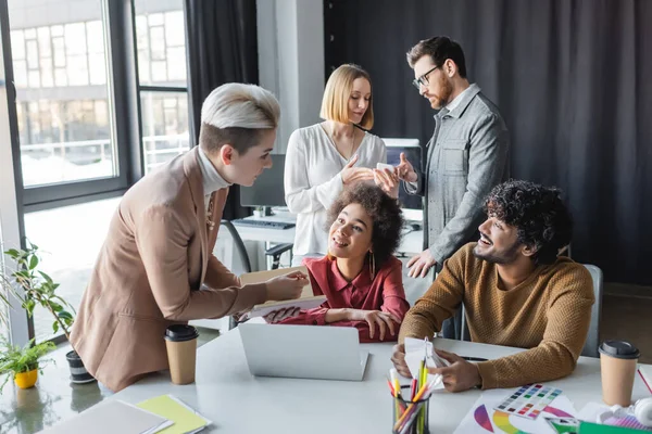 Femme avec ordinateur portable parlant à des designers interraciaux en agence de publicité — Photo de stock