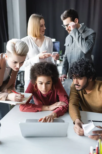 Concentrated african american woman using laptop near multiethnic colleagues in advertising agency — Stock Photo