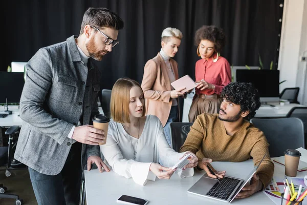 Indian man pointing at laptop near colleagues in advertising agency — Stock Photo