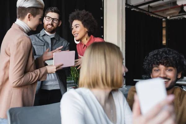 Smiling multicultural advertising managers talking near colleagues on blurred foreground — Stock Photo