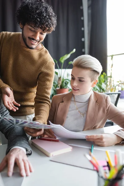 Positive indian advertising designer pointing at color samples near colleague in office — Stock Photo