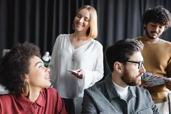 Mujer de negocios afroamericana sonriendo cerca de equipo multiétnico en agencia de publicidad - foto de stock