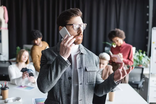 Directeur de la publicité dans les lunettes parler sur smartphone près de collègues multiculturels flous — Photo de stock