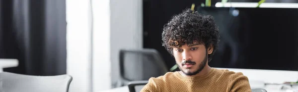 Young and curly indian man working in advertising agency, banner — Stock Photo