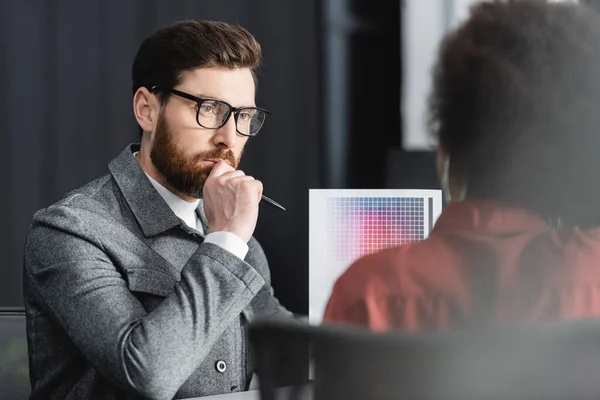 Hombre reflexivo mirando borrosa colega y muestras de color en la agencia de publicidad - foto de stock