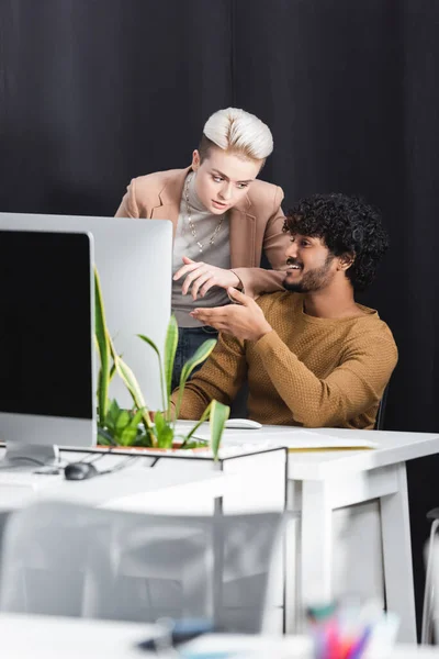 Diseñador indio feliz apuntando al monitor de la computadora cerca de administrador de publicidad - foto de stock