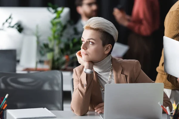 Thoughtful designer looking away in advertising agency near blurred colleagues — Stock Photo