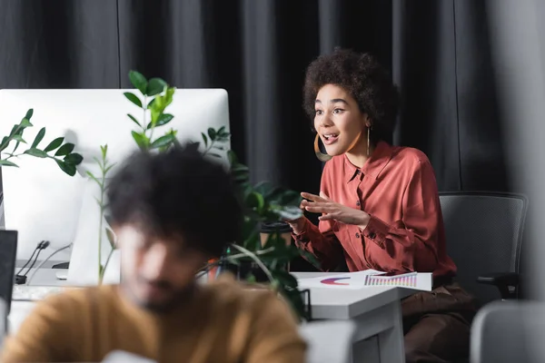 Amazed african american advertising manager gesturing during video call in office near blurred indian colleague — Stock Photo