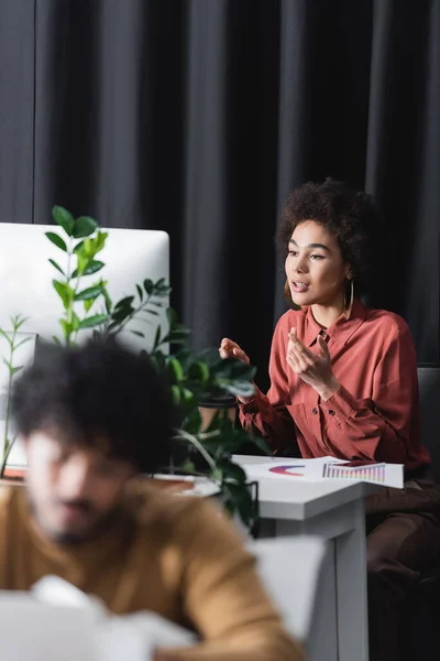 Afro-américain gestionnaire parler pendant le chat vidéo dans l'agence de publicité près flou homme indien — Photo de stock