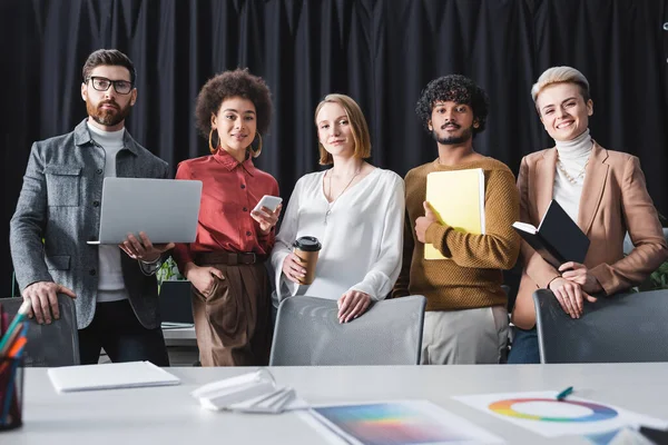 Equipe multiétnica positiva da agência de publicidade olhando para a câmera no escritório — Fotografia de Stock