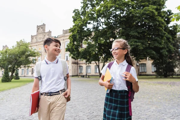 Позитивні міжрасові школярі з блокнотами, що виходять на вулицю — стокове фото