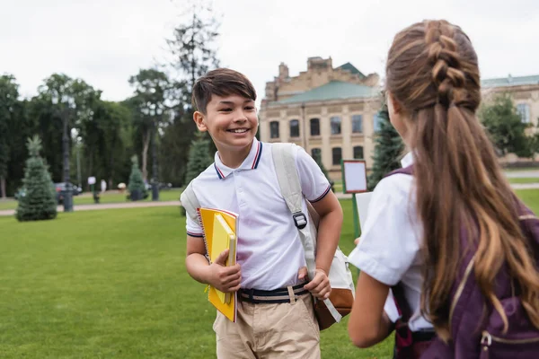 Positivo asiatico scolaro holding notebook vicino sfocato amico all'aperto — Foto stock