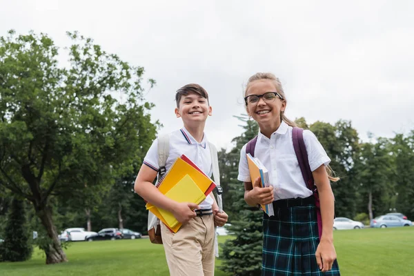 Happy multiethnic pupils with notebooks looking at camera outdoors — Stock Photo