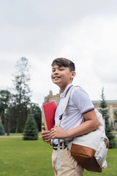 Sorrindo asiático estudante segurando notebook e mochila ao ar livre — Fotografia de Stock