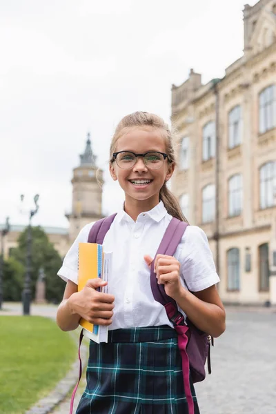 Colegiala sonriente en gafas con cuadernos al aire libre - foto de stock