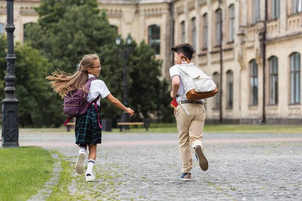 Улыбающаяся школьница бегает рядом с азиатской подругой на улице — стоковое фото