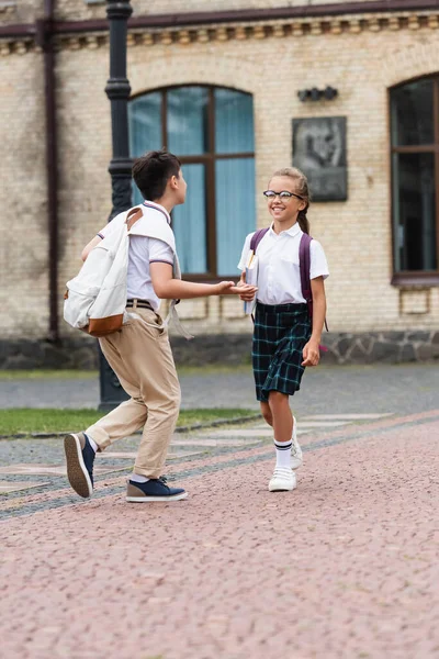 Asiatico scolaro con zaino parlando per allegro amico con notebook all'aperto — Foto stock