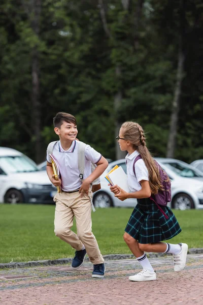 Multiethnic classmates with notebooks running outdoors — Stock Photo