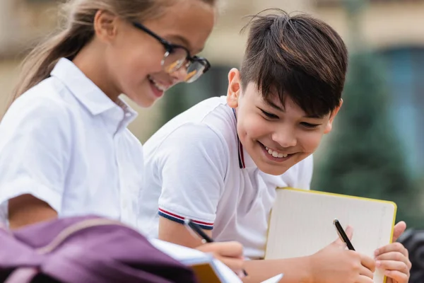 Positivo asiático escolar celebración pluma y portátil cerca amigo al aire libre - foto de stock