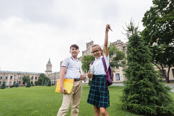 Interrassische Schüler mit Notizbüchern blicken auf dem Rasen in die Kamera — Stockfoto