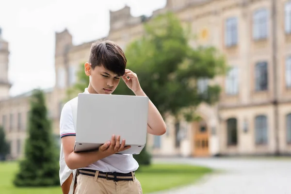 Pensive asian schoolboy looking at laptop outdoors — Stock Photo