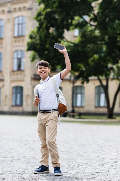 Positives asiatisches Schulkind mit Laptop und Smartphone im Freien — Stockfoto