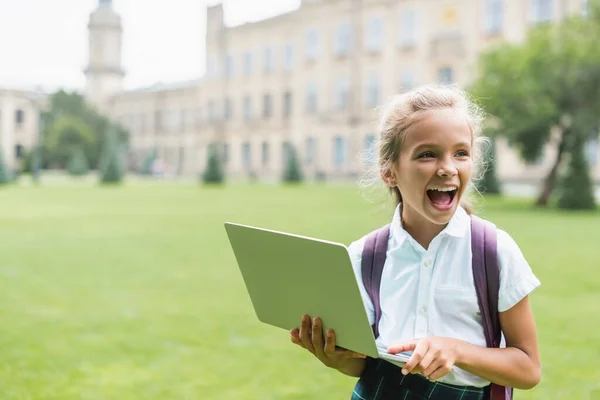 Emocionado colegiala sosteniendo portátil en el parque - foto de stock