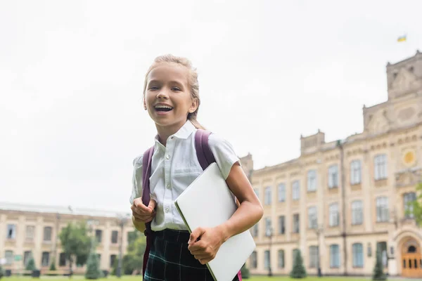 Preteen schoolkid with Rucksack holding laptop and looking at camera outside — Stockfoto