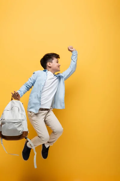 Vue latérale de l'écolier asiatique tenant le sac à dos et sautant isolé sur jaune — Photo de stock