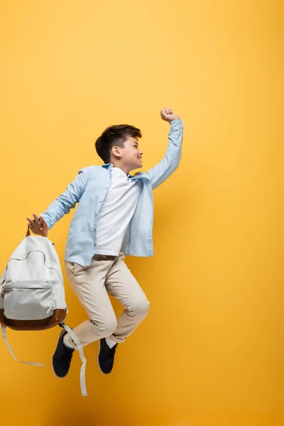 Vista laterale di asiatico scolaro holding zaino e jumping isolato su giallo — Foto stock