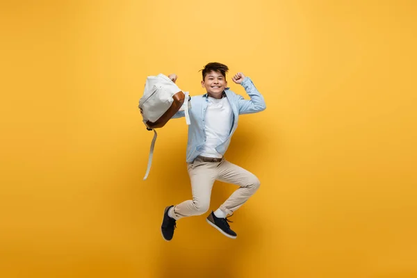 Joyeux asiatique écolier tenue sac à dos et saut sur jaune fond — Photo de stock