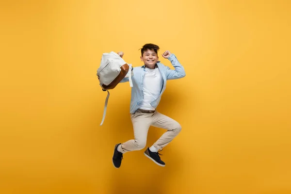 Alegre asiático escolar celebración mochila y saltar en amarillo fondo — Stock Photo
