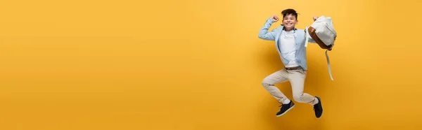 Emocionado asiático escolar celebración mochila y saltar sobre amarillo fondo, bandera - foto de stock