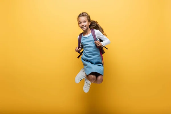 Happy preteen schoolgirl with backpack jumping on yellow background — Stock Photo